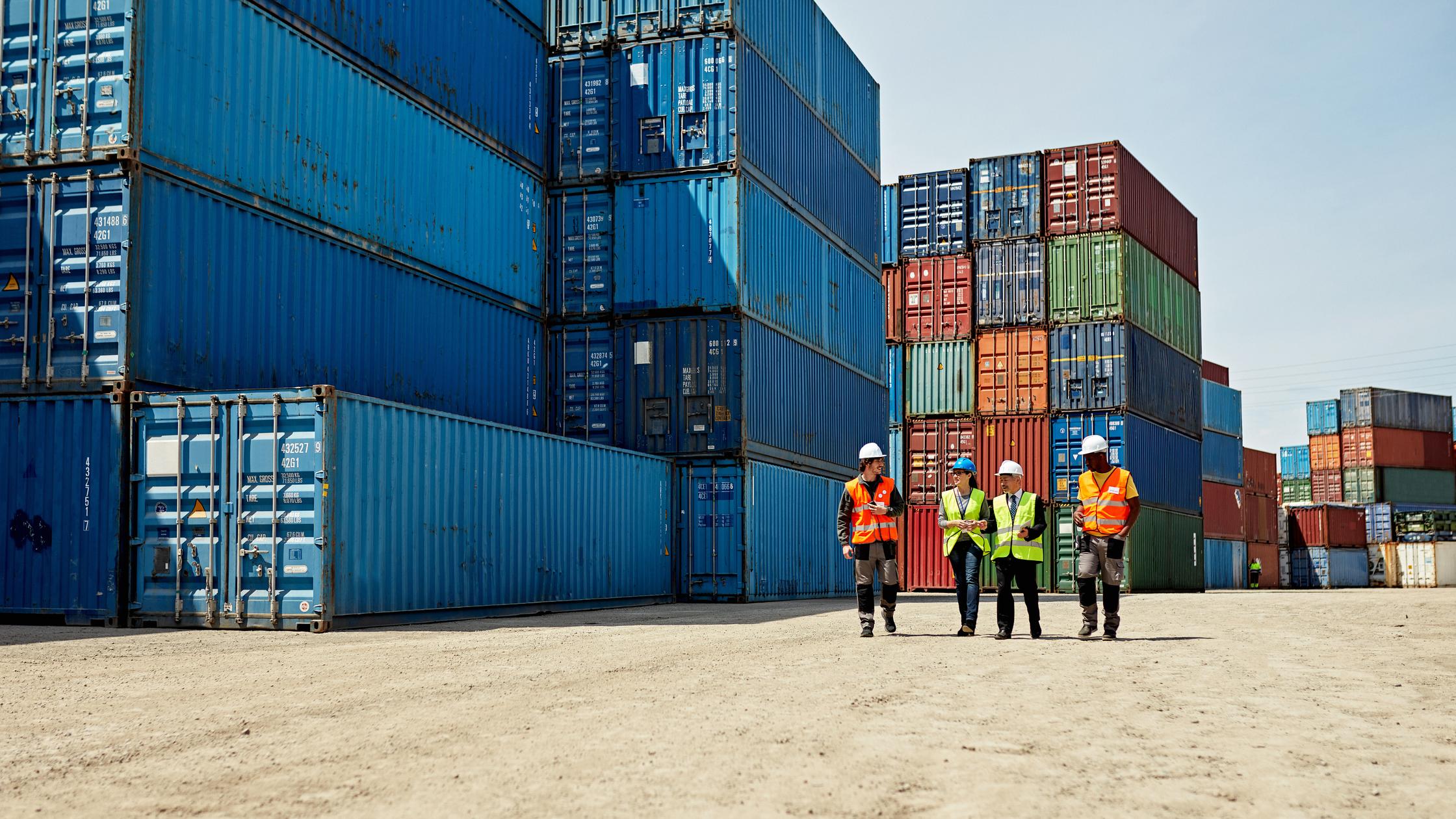 Supply Chain - People in hard hats amidst stacks of cargo containers
