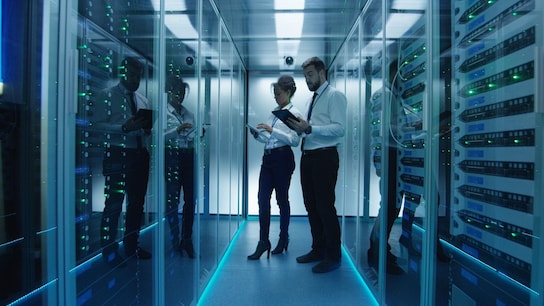 Side view of a man and a woman with tablets coworking in data center server room checking hardware