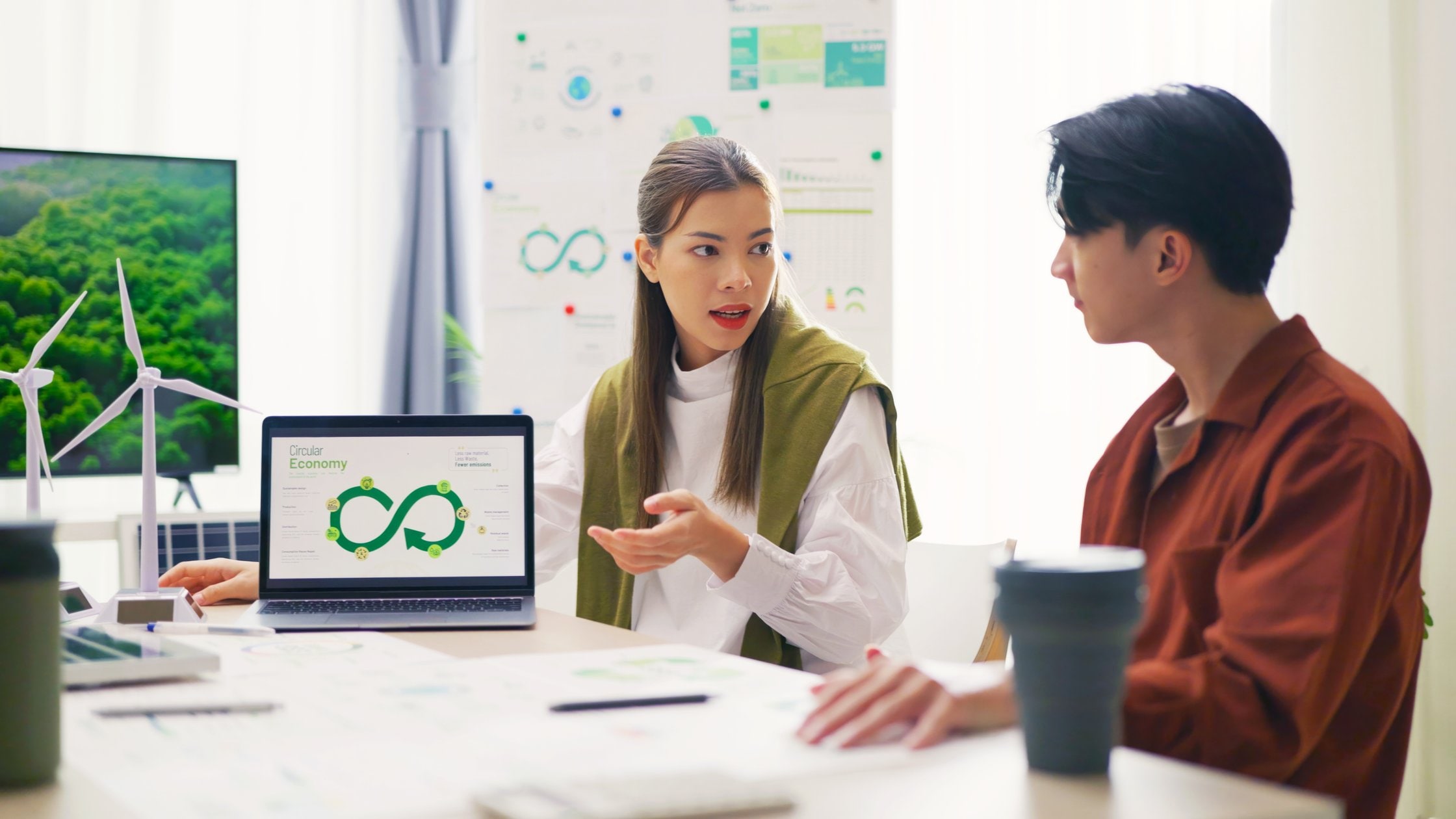 A team of professionals, including a focused woman, discusses Environmental, Social, and Governance (ESG) strategies using a laptop presentation in a bright office.